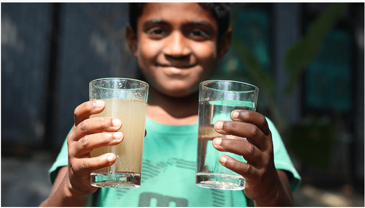 A boy holding two glasses of water - one brown and muddy, one clear and clean. 